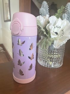 a pink and purple cup sitting on top of a wooden table next to a vase with flowers