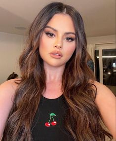 a woman with long brown hair wearing a black shirt and red cherries on her chest