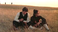 two people sitting on the ground in tall grass, one holding a plate and looking down