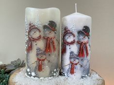 two snowman candles sitting on top of a tree stump covered in snow next to each other