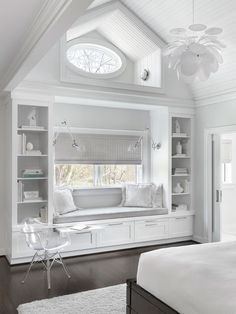 a white bedroom with built in bookshelves and window seat on the far wall