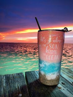 a cup sitting on top of a wooden table next to the ocean with a straw in it