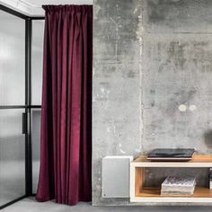 a room with concrete walls and red drapes on the window sill, next to a shelf with books