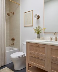 a white toilet sitting next to a bath tub in a bathroom under a framed picture