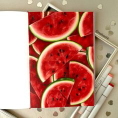 an open notebook with watermelon slices on it next to markers and pencils