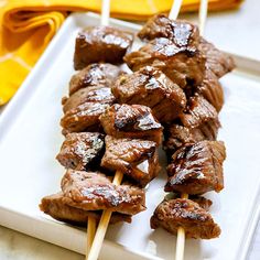 several skewers of meat sitting on top of a white plate with yellow napkins