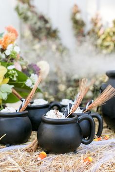 three black mugs sitting on top of hay with flowers in the backgroud