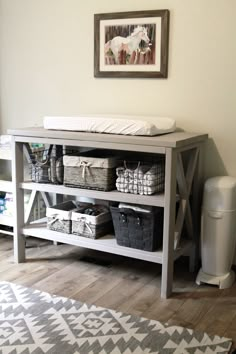 a baby changing table with baskets and blankets on it in the corner of a room