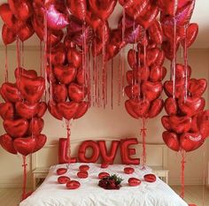 a bed with lots of red heart shaped balloons hanging from the ceiling