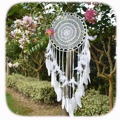 a white dream catcher sitting on top of a lush green field next to trees and flowers