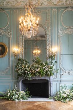 an ornate room with blue walls and chandelier above the fireplace, decorated with flowers