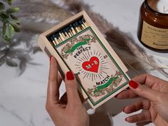 a person holding a match box with matches in it next to a candle and some feathers