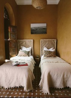 two twin beds in a room with yellow walls and patterned flooring, one has a painting on the wall