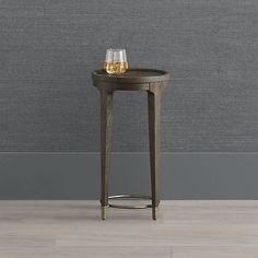 a small table with a glass on it next to a gray wall and wooden floor