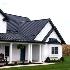 a white house with black shingles on the roof and front porch, along with a blue door