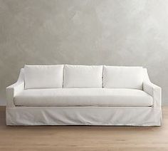 a white couch sitting on top of a hard wood floor next to a gray wall