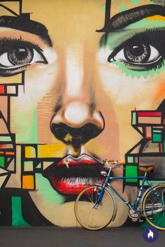 a bicycle parked in front of a colorful wall with a woman's face painted on it