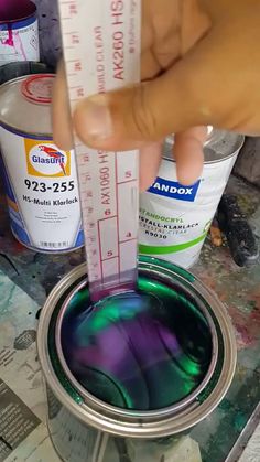 a person is holding a paint roller and painting the inside of a can with purple and green colors