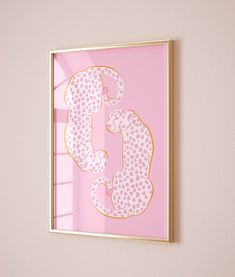 a pink wall with a gold framed letter and polka dot pattern on it, in front of a window