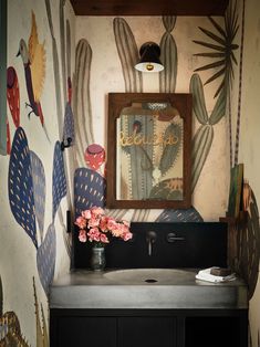 a bathroom with cactus wallpaper and a mirror above the sink, along with a vase filled with pink flowers