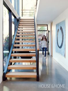 a woman walking down a hallway next to a set of wooden stairs with handrails