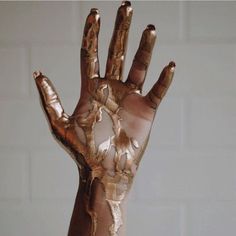 a person's hand with gold paint on it and white brick wall in the background