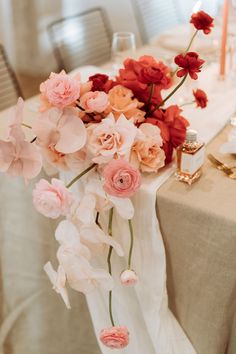 a table topped with pink and red flowers on top of a white cloth covered table