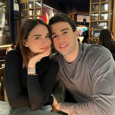 a man and woman sitting next to each other at a table in front of a bar