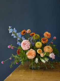 a vase filled with colorful flowers on top of a wooden table next to a blue wall