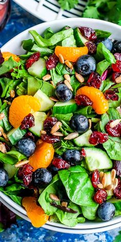 a salad with oranges, blueberries and spinach in a white bowl on a table