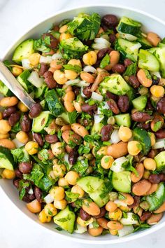 a white bowl filled with beans, cucumbers and other veggies next to a spoon