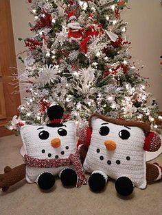 two crocheted snowmen sitting in front of a christmas tree