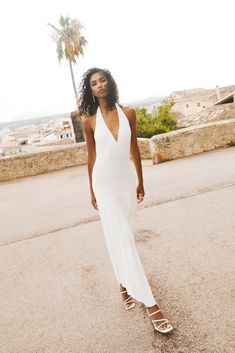 a woman in a white dress is standing on the street with palm trees behind her