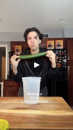 a man holding up a cucumber in front of a cup with the words making a cucumber salad on it