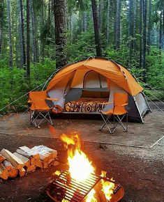 an orange tent sitting in the middle of a forest next to a campfire with logs