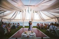 a bride and groom standing under a white draping at their wedding reception by the ocean