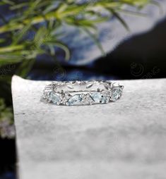 an image of a wedding ring with blue topazte stones on the surface next to a potted plant