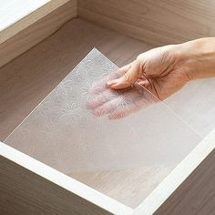 a person's hand reaching for a piece of clear plastic in a drawer with wood trim