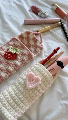 some crocheted items are laying out on a white sheet with pens and pencils