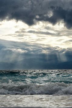 the sun shines through clouds over the ocean as waves crash in front of it