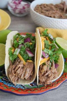 two tacos with meat, onions and cilantro on a colorful plate next to lime wedges