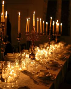 a long table with many lit candles and plates on it, all set up for a formal dinner