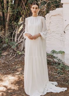 a woman wearing a white dress standing in front of trees