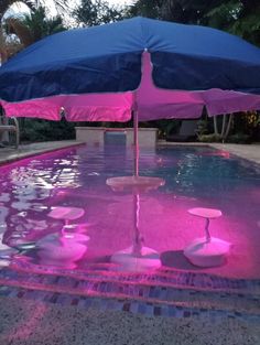 an umbrella that is in the water near some rocks and plants with pink lights on it