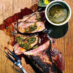 some meat is sitting on a wooden table next to a bowl of sauce and utensils