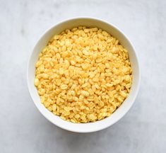 a white bowl filled with yellow cereal on top of a counter next to a spoon