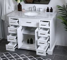 a white bathroom vanity with drawers and a mirror above it, next to a potted plant