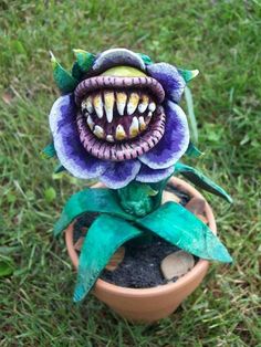 a fake flower with teeth on it sitting in a pot filled with dirt and grass