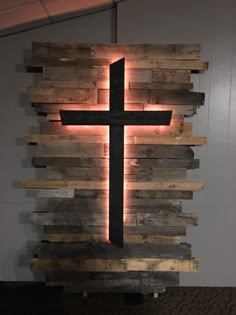 a cross made out of wooden planks is lit up by lights on the wall