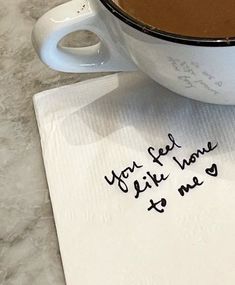 a cup of coffee sitting on top of a table next to a napkin with writing